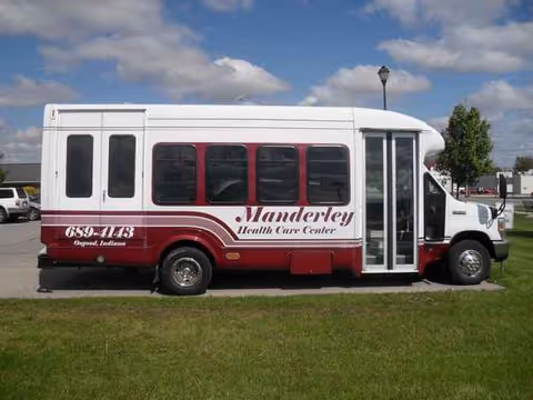White and maroon Manderley Health Care Center bus parked on a grassy lot