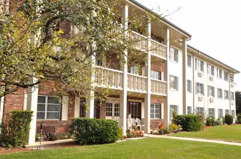 Three-story apartment building with brick accents, balconies, and a manicured lawn.