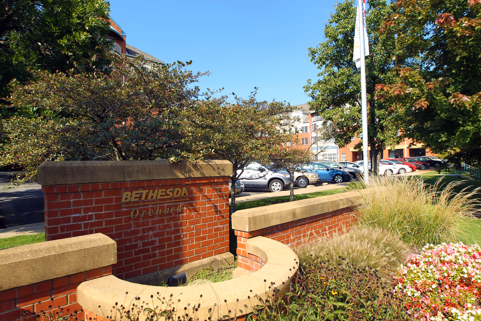 Brick entrance sign reading 'BETHESDA Orchard' surrounded by landscaping with parked cars and the facility building visible behind.