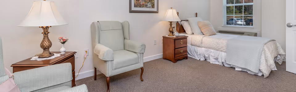 A furnished bedroom with a single bed, two nightstands with lamps, and upholstered armchairs.