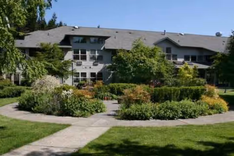 Two-story gray senior living building framed by a circular landscaped walkway.