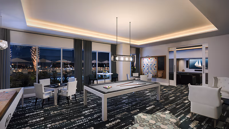 Modern game room with a pool table, multiple seating areas, large windows showing a nighttime view, and recessed ceiling lighting.