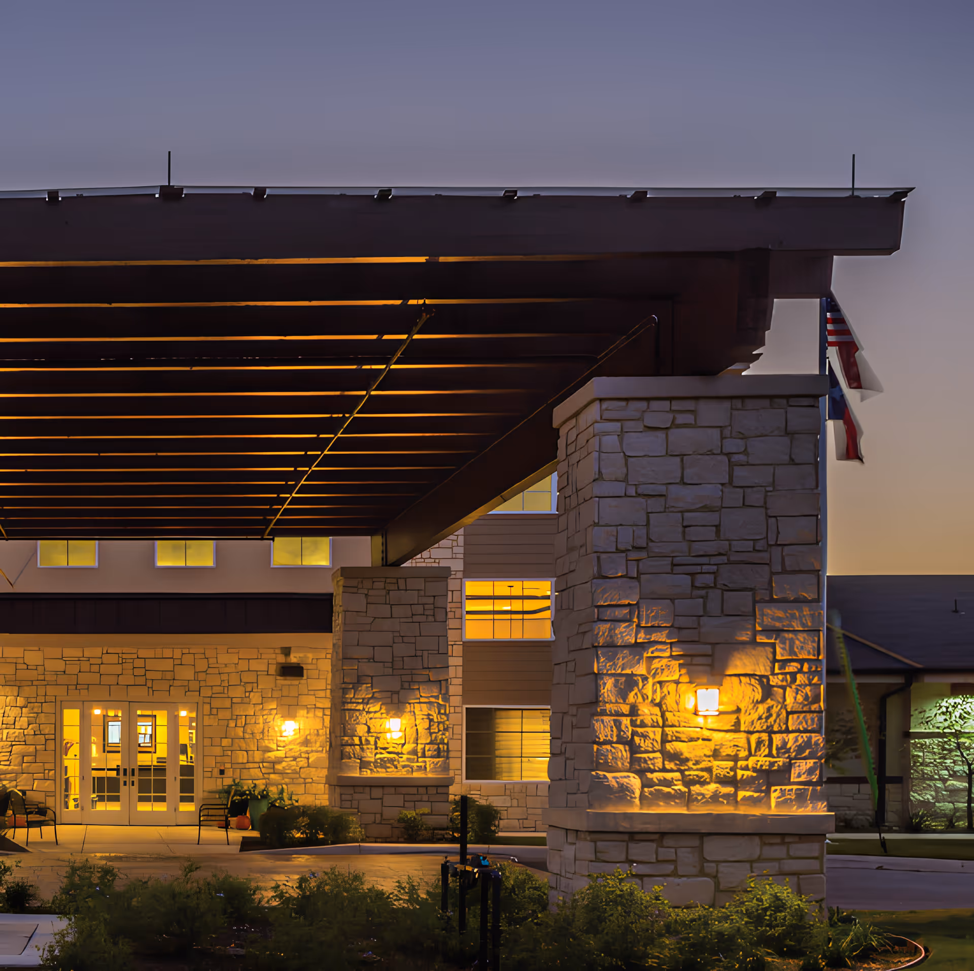 Covered entrance with a large wooden canopy, stone pillars, and warm exterior lighting at dusk.