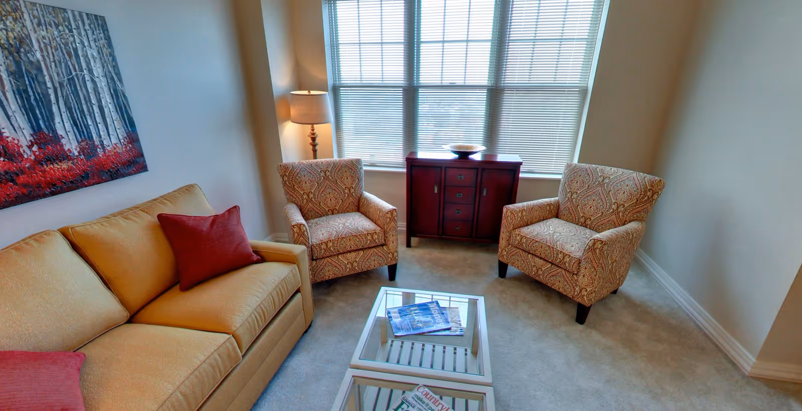 Cozy living room with a yellow sofa, two patterned armchairs, a coffee table and a cabinet under a large window.