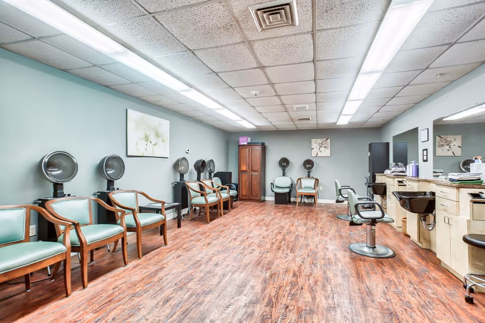 Interior view of a hair salon with styling chairs, hairdryers, and wooden flooring.