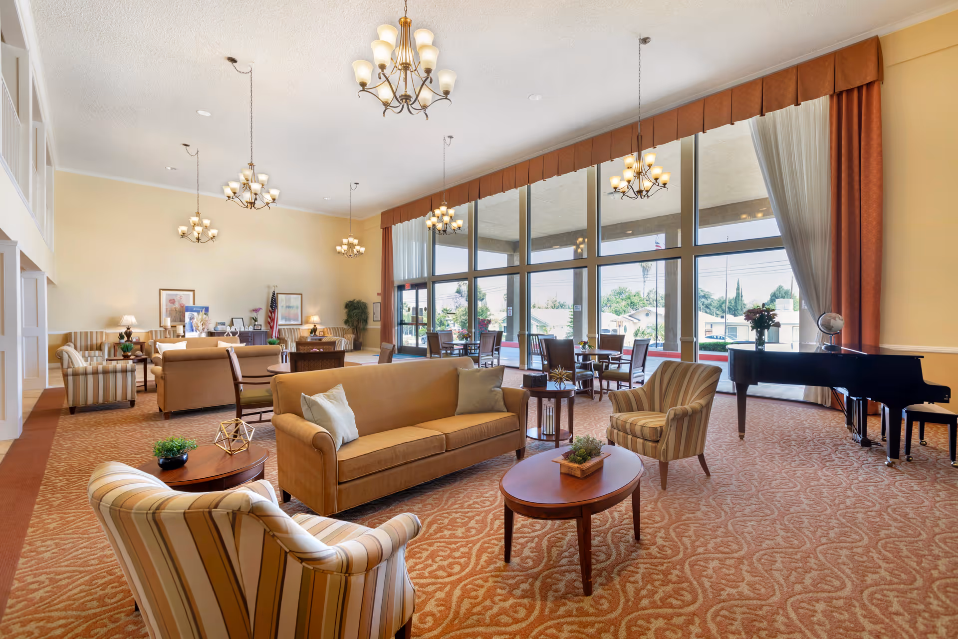 Spacious senior living facility lounge with sofas, armchairs, coffee tables, chandeliers, floor-to-ceiling windows and a grand piano.