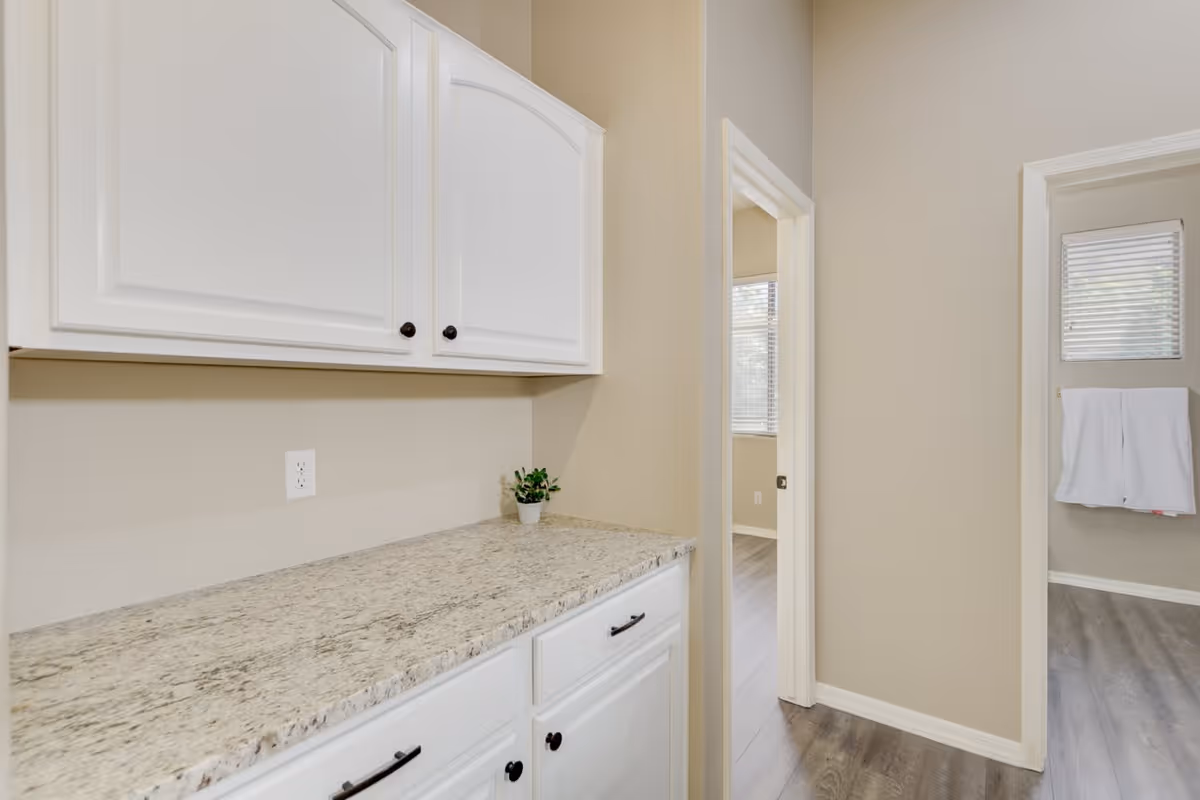 Built-in white cabinets and a granite countertop in a beige interior hallway with doorways to adjacent rooms.