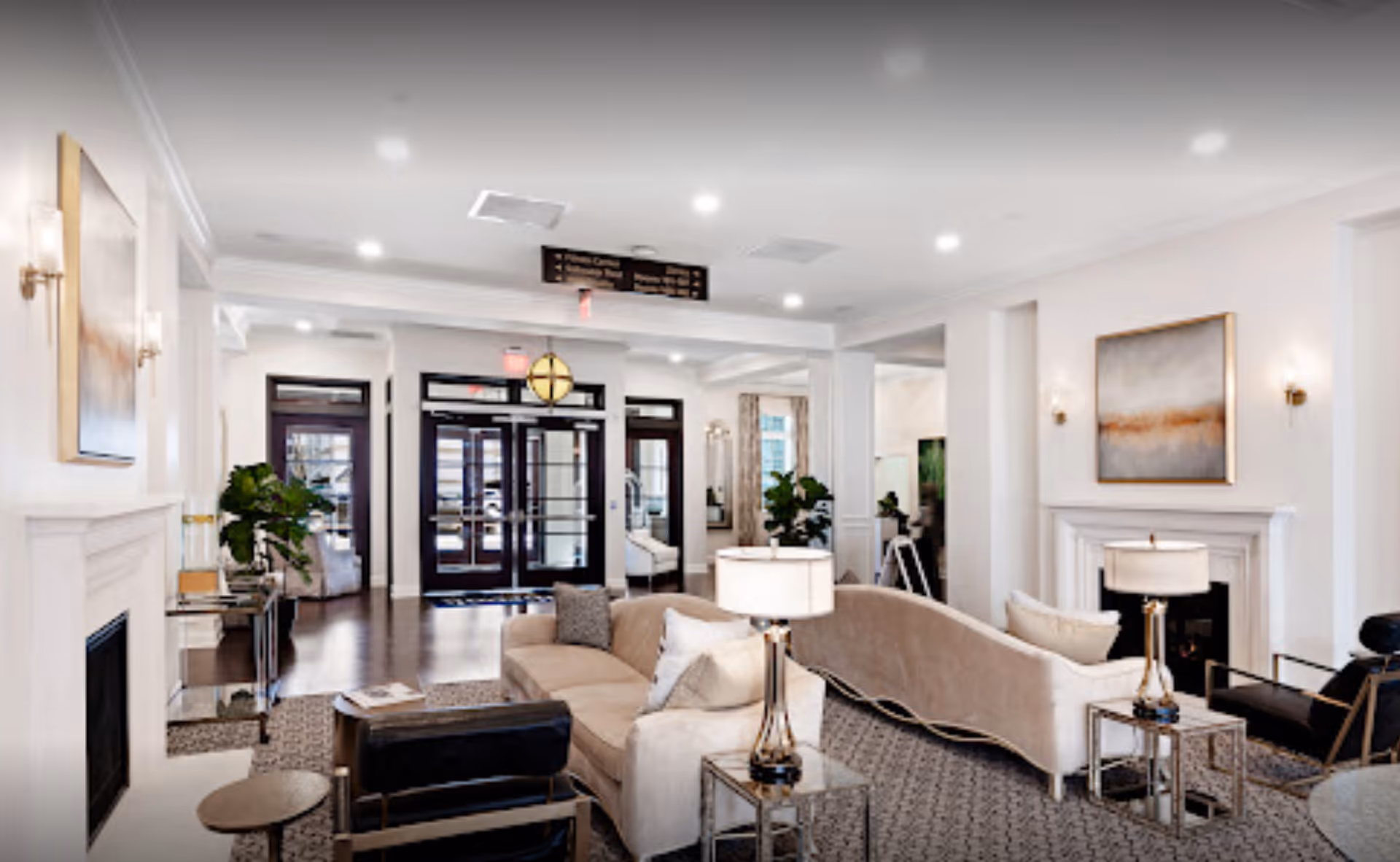 Bright, elegant lounge with sofas, armchairs, lamps and a fireplace leading to glass entry doors.