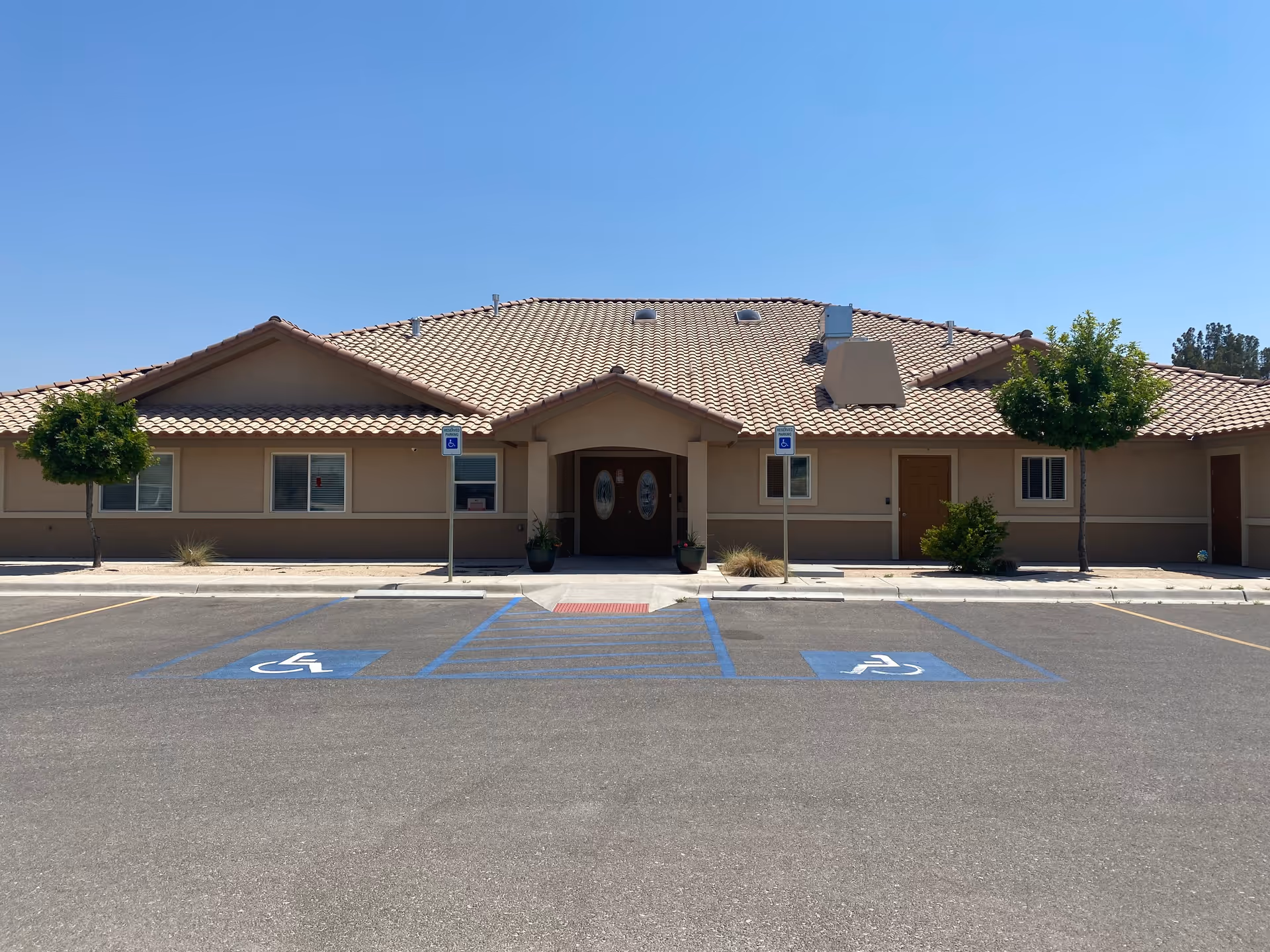 Front exterior of a single-story senior living building with a tiled roof, central entrance and handicap parking spaces in the foreground.