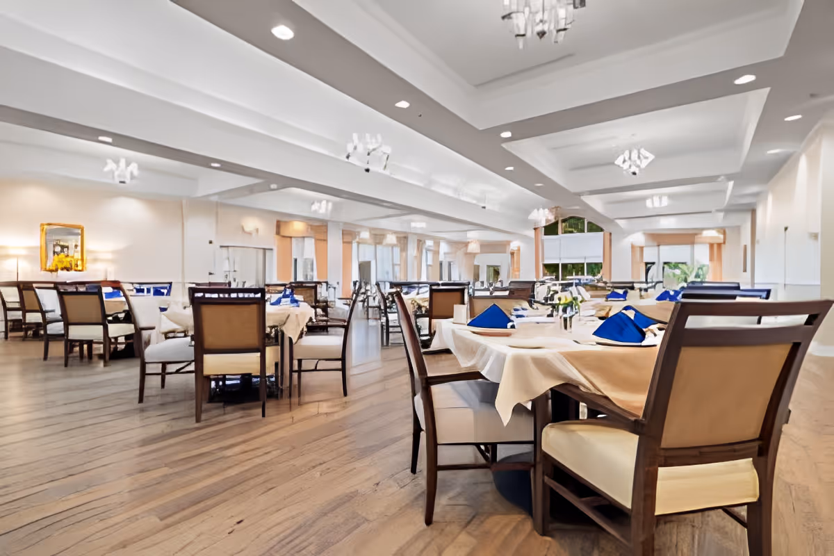 Spacious, well-lit dining room with multiple set tables, wooden chairs, and chandeliers under a coffered ceiling.