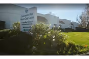 Exterior view of Chatsworth Park Health Care Center building with a sign in front surrounded by bushes and a well-maintained lawn under a clear sky.
