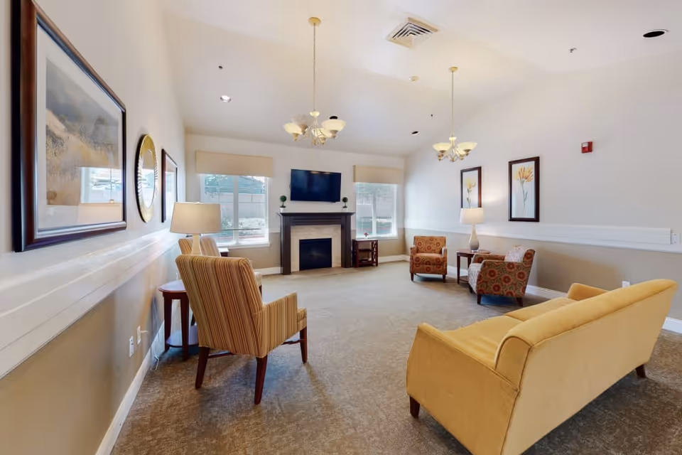 Bright common sitting room with sofas and armchairs arranged around a fireplace and wall-mounted TV.