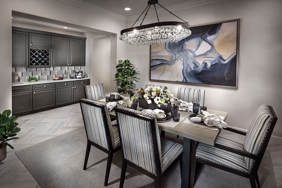 A modern dining room with a table set for six beneath a crystal chandelier and built-in cabinetry in the background.