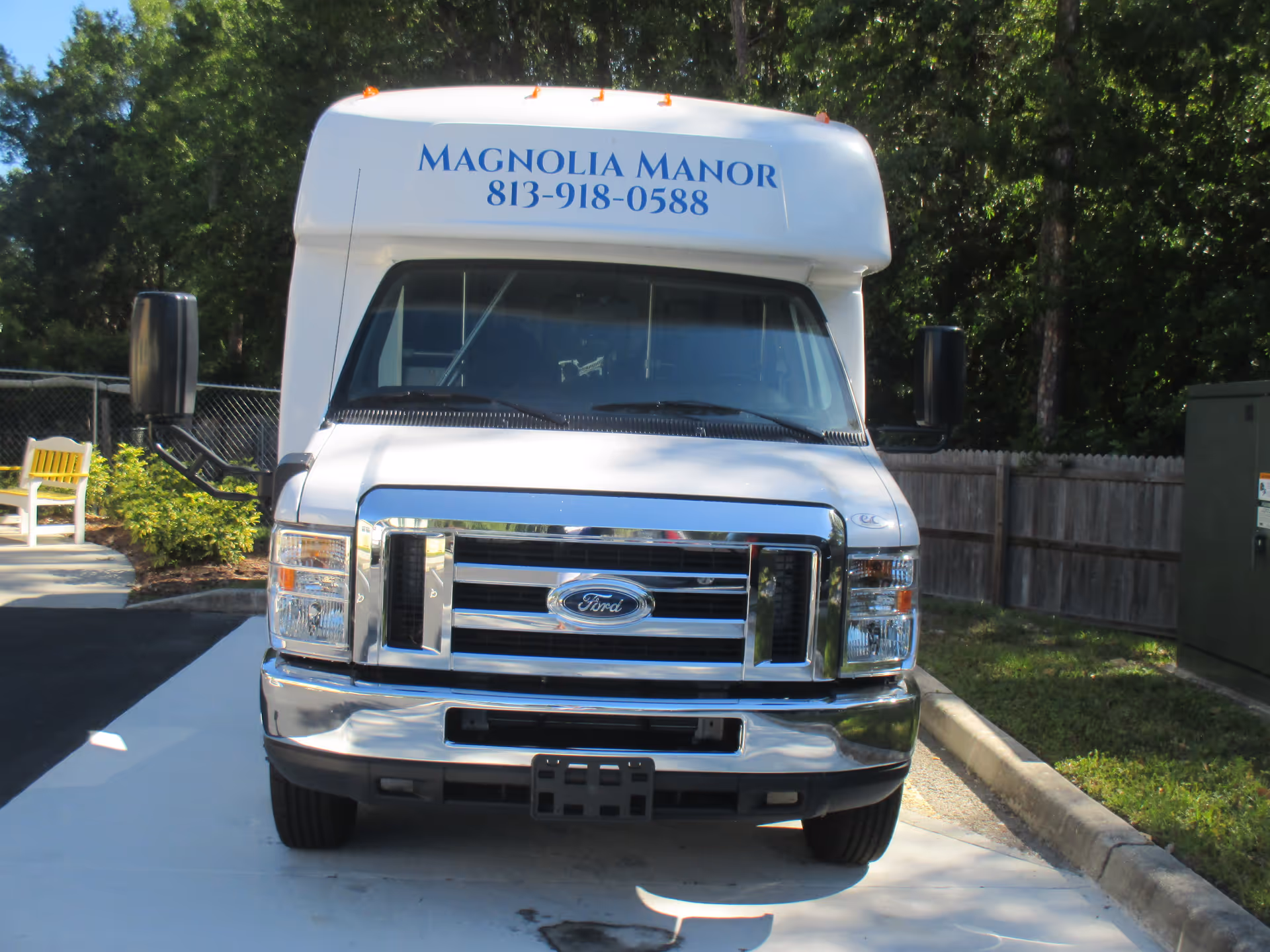 Front view of a white Magnolia Manor shuttle van parked outside with its name and phone number on the roof.