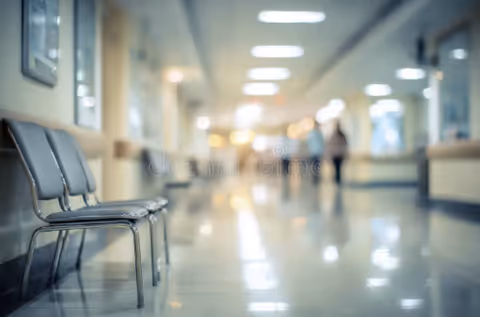 Bright interior hallway of a senior living facility with a row of chairs along the left and blurred figures in the background.