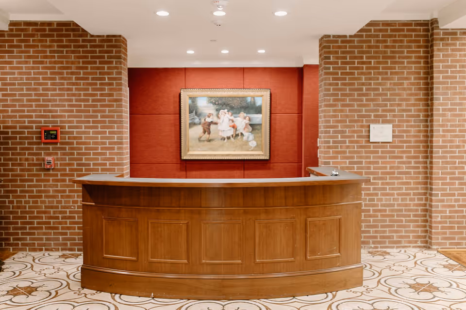 Wooden curved reception desk in a brick-walled lobby with a framed painting on red paneling behind it.