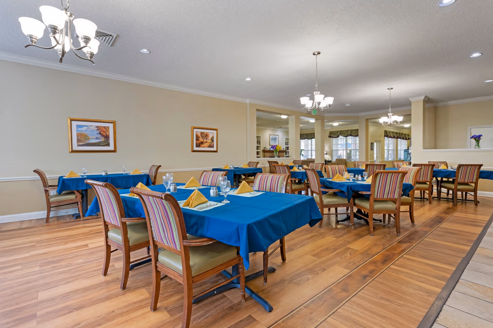 Spacious dining room with several tables draped in blue tablecloths, place settings, and striped chairs.