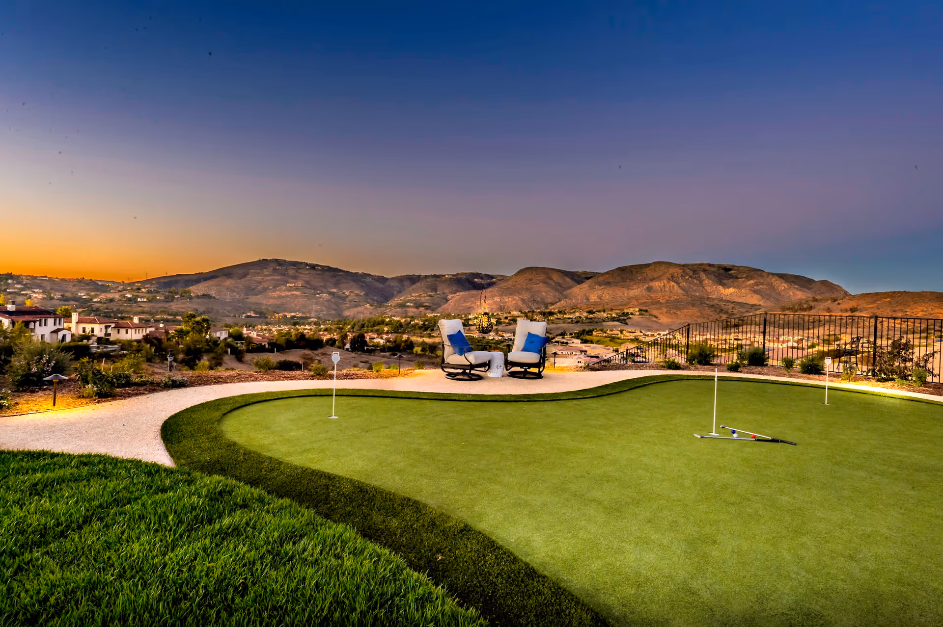 Outdoor putting green with two lounge chairs overlooking rolling hills at sunset.