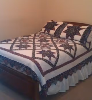 A neatly made bed with a patchwork quilt in a small bedroom.