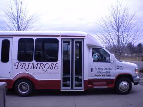 White Primrose shuttle bus parked outdoors beside bare trees.