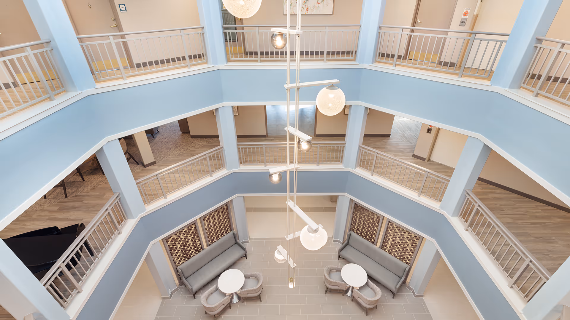 Open multi-level atrium with pale blue walls, hanging globe lights and seating areas with sofas and round tables.