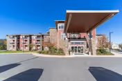 Exterior view of a multi-story senior living facility named The Summit, featuring a large covered entrance with stone and brick accents, multiple windows, and a paved driveway in front.