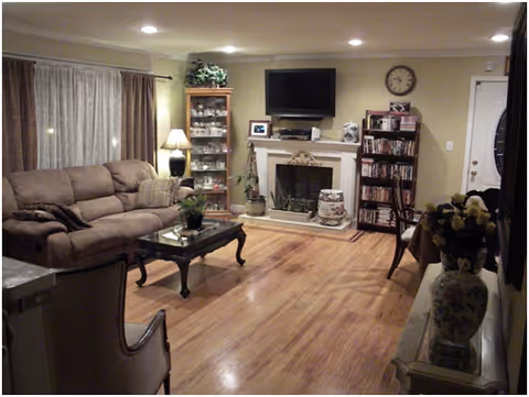 Cozy living room with sofa, coffee table, fireplace, TV, and bookshelves in a senior living facility.