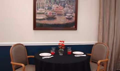Round dining table with place settings and a floral centerpiece in a senior living dining room.