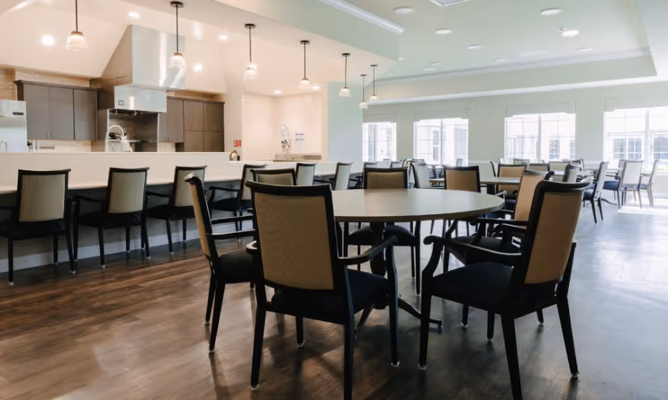Bright communal dining area with round tables and chairs and an open kitchen with a long breakfast bar and pendant lights.