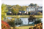 Scenic view across a pond showing residential buildings, a fountain, and landscaped grounds.