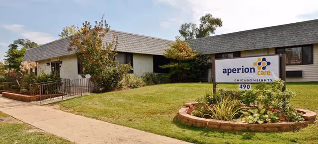 Exterior view of Aperion Care Chicago Heights building with a lawn and landscaped garden in front, featuring a sign with the facility name and address number 490.