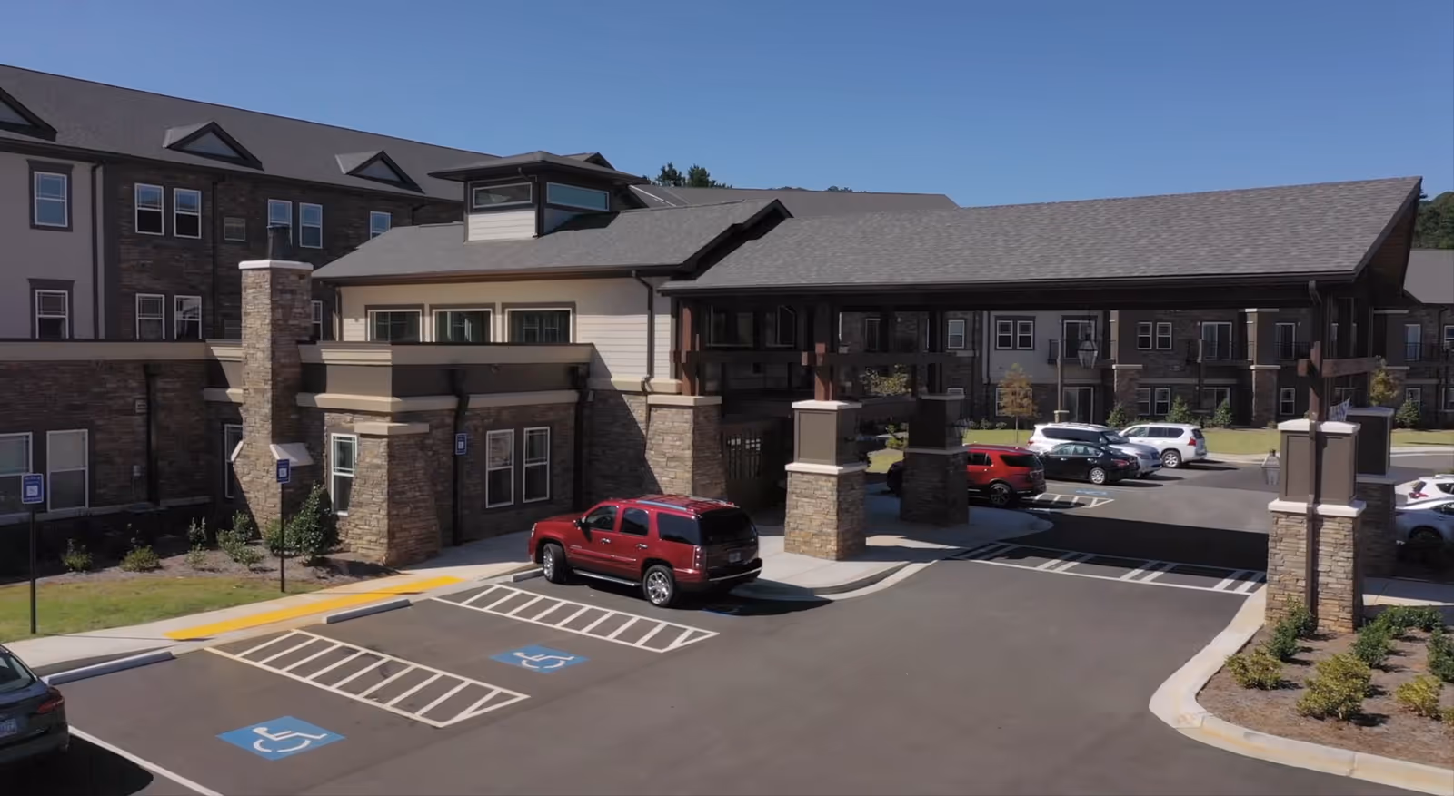 Front entrance of a senior living building featuring a large covered porte-cochere with stone pillars and adjacent parking including handicap spaces.