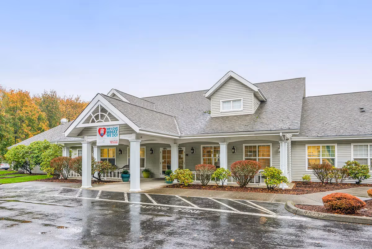 Front exterior of a single-story senior living building with a covered entrance, columns, and landscaped shrubs.