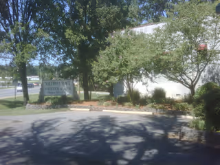 Outdoor view of the Retirement Center of Arkansas showing a parking area, trees, bushes, and a sign with the facility's name and phone number.