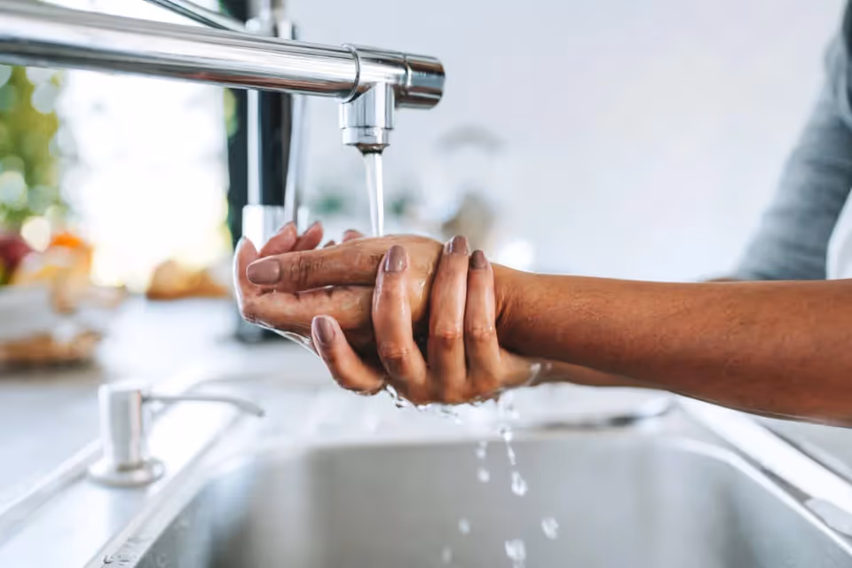 Hands being washed under a running faucet at a modern kitchen sink.