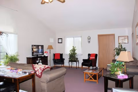 Cozy senior living room with couches, chairs, plants, and a TV.