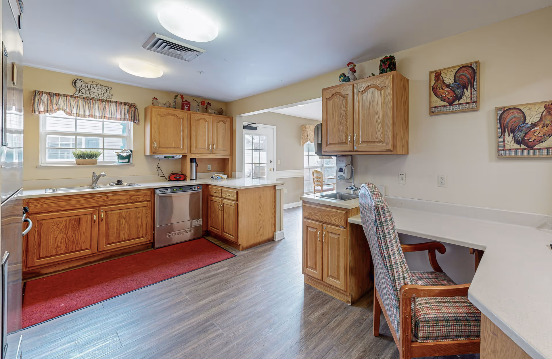 Bright residential-style kitchen with oak cabinets, stainless dishwasher, sink, countertops, and a chair at a built-in counter.