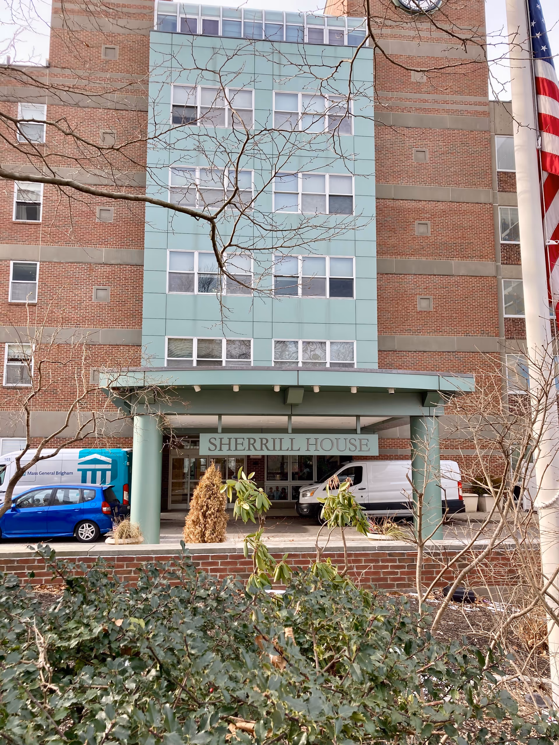 Front entrance of the Sherrill House building with a canopy sign, parked vehicles, and shrubs in the foreground.