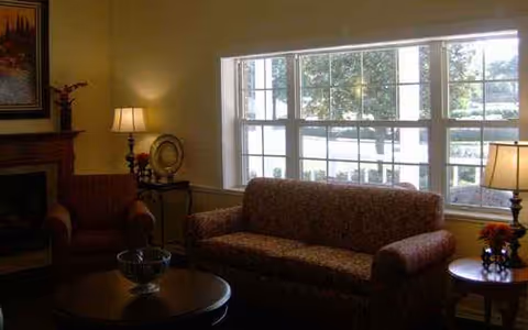 Cozy living room with sofa, armchairs, lamps, fireplace, and a large window.