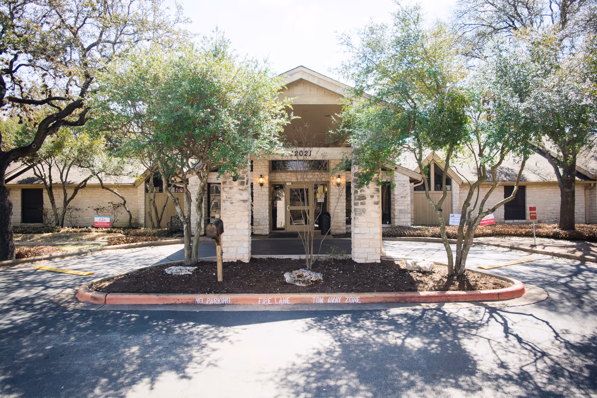 Front entrance of a nursing center with a covered stone portico, trees, and a circular driveway.