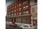 Brick multi-story Hotel Pennsylvania Apartments building on a city street with parked cars.
