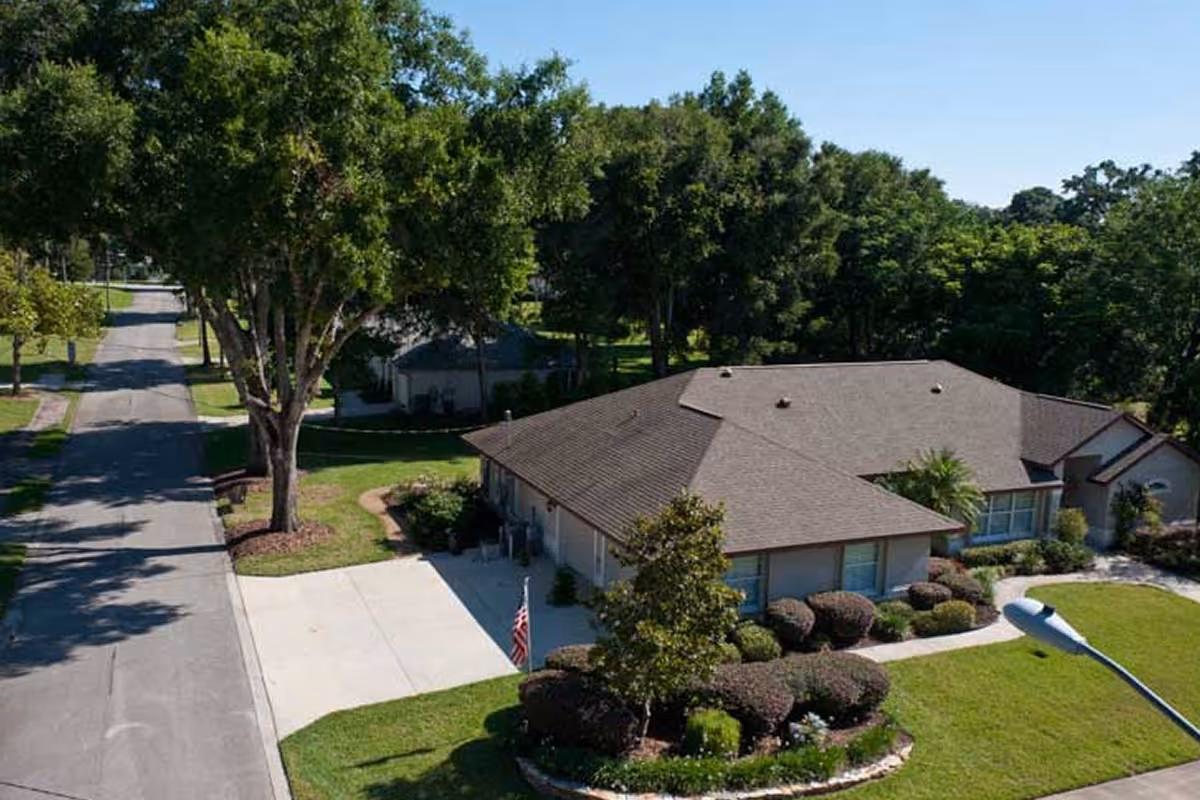 Aerial view of a single-story senior living facility with a landscaped front yard, driveway and surrounding trees.
