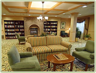 Comfortable lounge with a striped sofa, green armchairs, a coffee table with a chessboard, bookshelves and a fireplace.