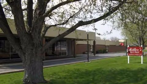 Exterior view of Miller's Merry Manor with a large tree and red sign.