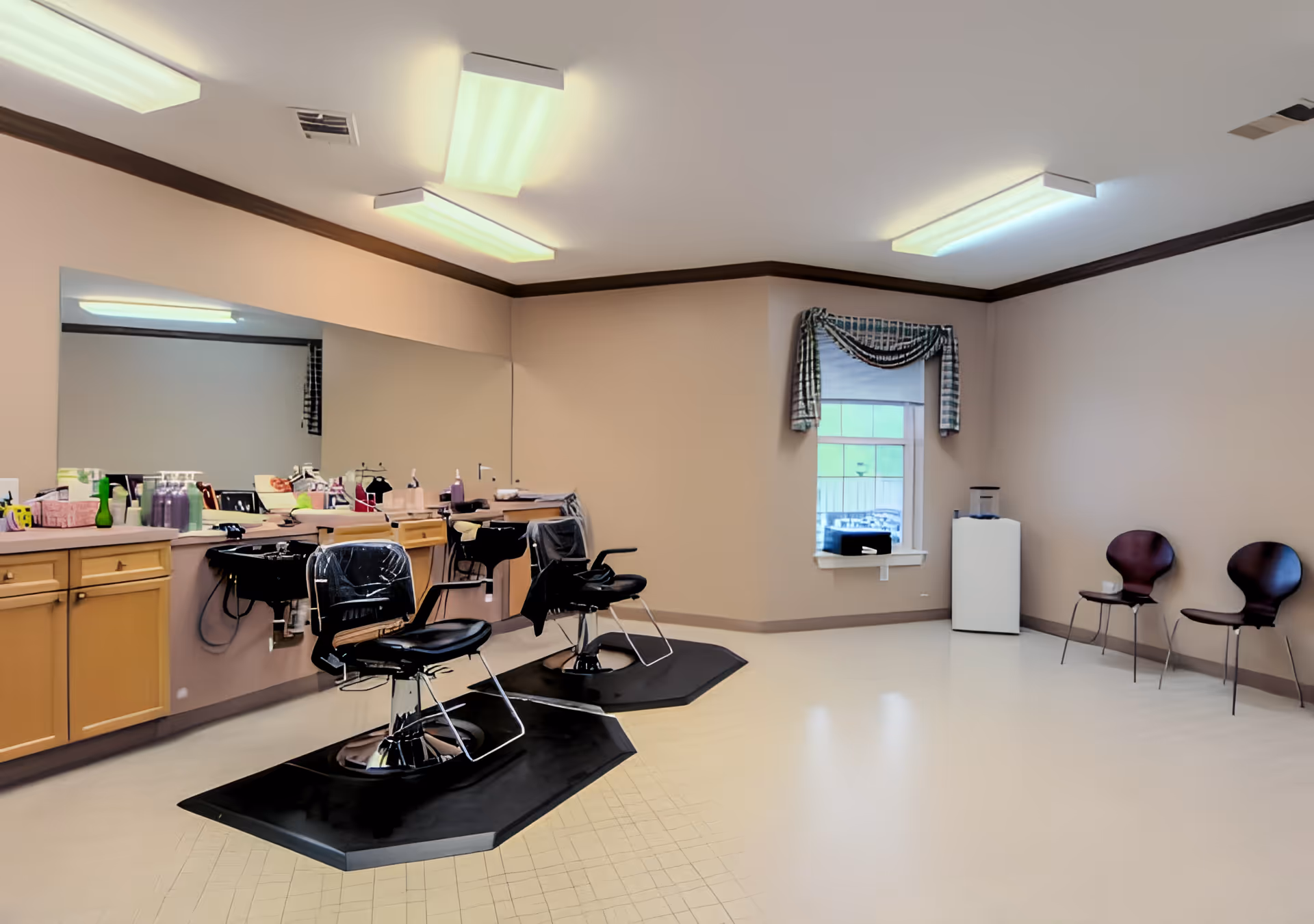 Interior salon with two barber chairs, large mirror and styling stations in a senior living facility.
