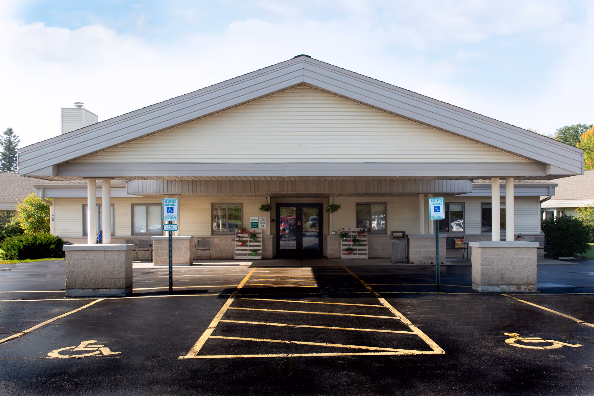 Front entrance of a single-story senior care facility with a covered porte-cochere and marked accessible parking spaces.