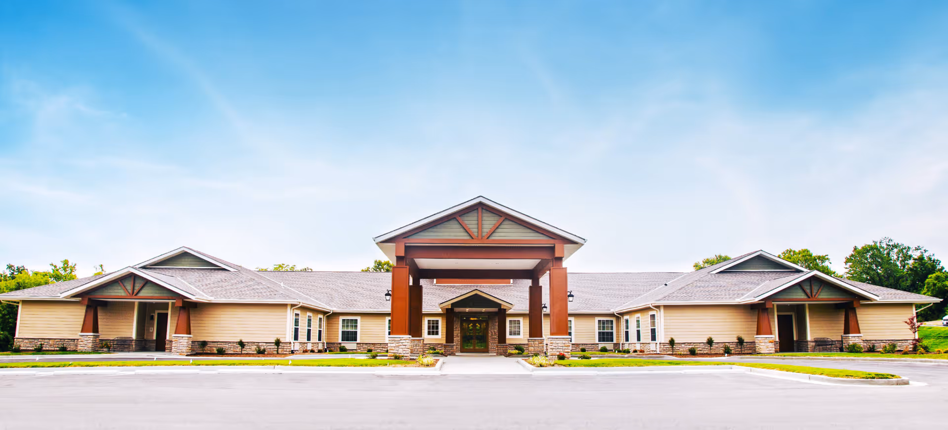 Wide front view of a single-story building with a large covered entrance, landscaped beds, and a clear blue sky.