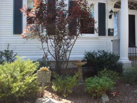 Front exterior of Wadleigh House Assisted Living, a white house with a porch and surrounding shrubs.