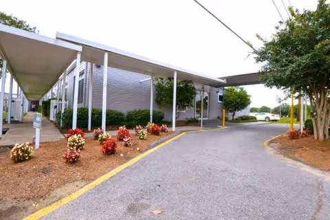 Exterior view of Metairie Health Care Center with a covered walkway, driveway, and landscaping.