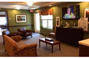 A cozy common lounge with sofas, armchairs, a coffee table, a television, and windows.